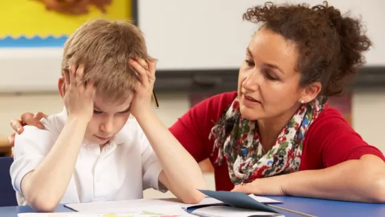 child holding his head in both palms while teacher speaks with him in class