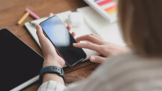 Pair of female hands using a mobile phone, above a desk.