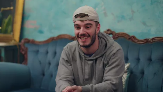 Young man sat on sofa, leans forward toward the camera engaged in conversation.