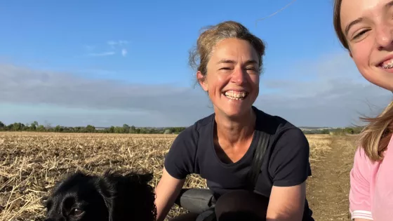Woman wearing a black t-shirt and girl in pink, probably Mum and daughter smile at the camera with a blue sky and cornfield back drop.daughter 