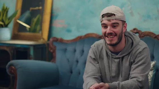 Young man sat on sofa, leans forward toward the camera engaged in conversation.