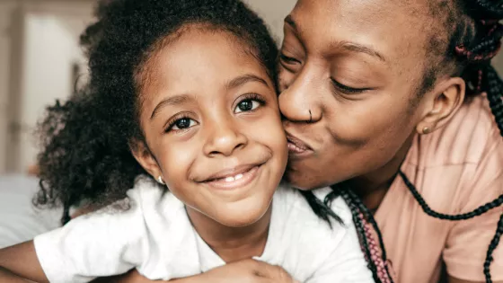 Mum kisses young daughter on the cheek, daughter smiles at the camerai