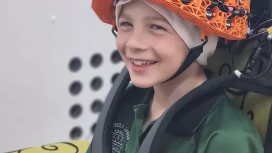 Young boy smiles at camera wearing an orange OPM-MEG helmet