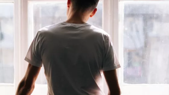 The back view of a young man looking out of the window in comtemplation.