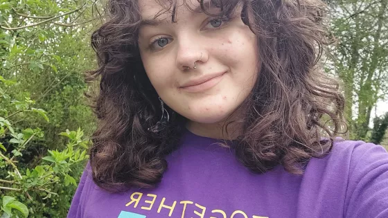 A young woman smiles in a selfie while wearing a 'together we create possible' Young Epilepsy t-shirt.
