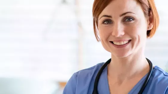 Female doctor in blue uniform smiles at the camera with her arms folded