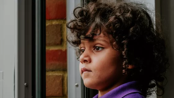 Young boy with soft dark curly hair looks out of the window