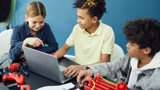 Two boys and one girl sit at a table with a laptop and other equipment participating in a focus group