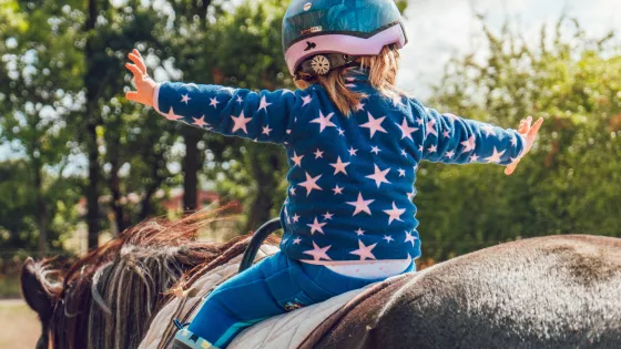 The back view of a young child on a horse with their arms spread