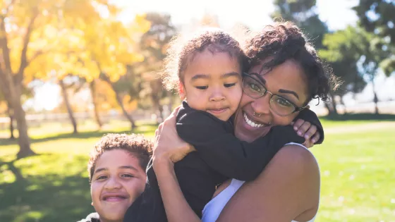 Young mum is holding one child, with other by her side - all smiling at the camera