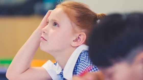 young pupil facing front of classroom, leaning her head on her hand concentrating