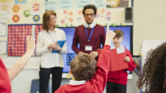 Photo of school students raising their hands in a classroom