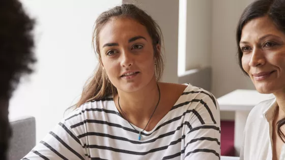 Two women look at and listen to a third person, who is pictured from behind, smiling slightly.