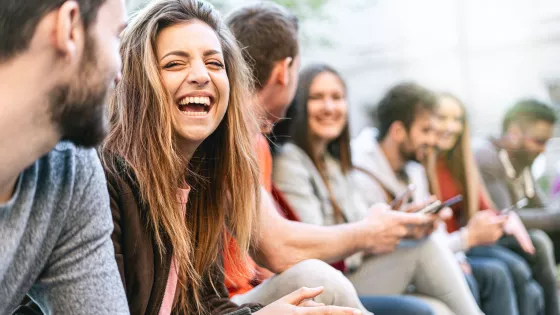 Online Youth Clubs: Group of trendy young people chatting together sitting on a bench outdoors. Students having fun together.