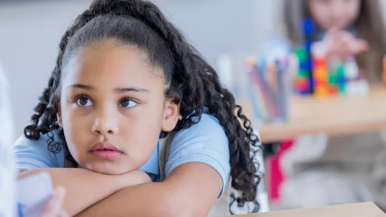 Photograph of young girl wearing school uniform leaning on a desk concentrating