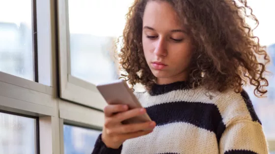 A young girl is looking at her mobile phone, looking sombre. 