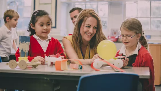 A teacher laughs alongside her students in a classroom.