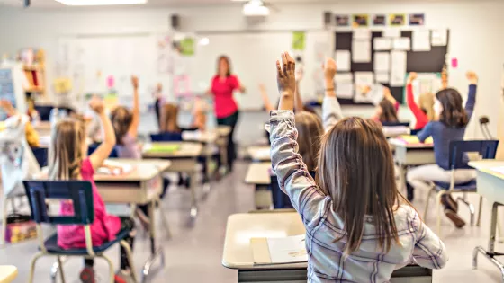 School children in a classroom with their hands up