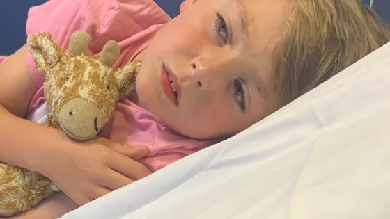 young boy lying on a hospital bed cuddling a giraffe