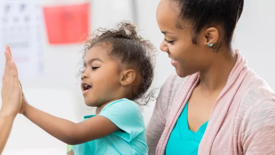 Nurse giving a child a high five whilst she sits on her mums lap