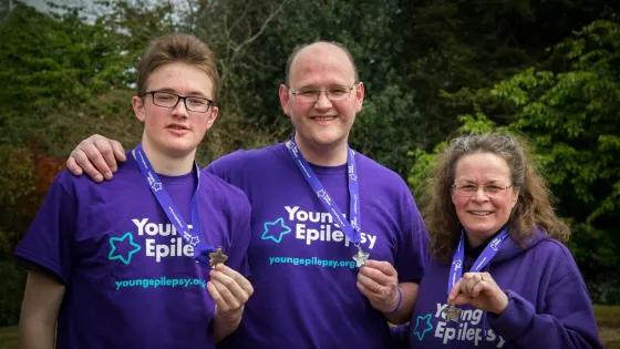 A young man and his parents smile while wearing Young Epilepsy t-shirts and medals.
