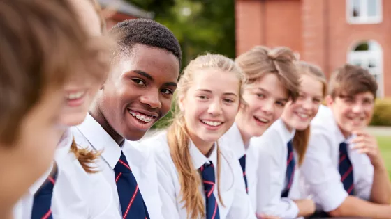 A group of students in shirts and ties sit on a wall smiling to camera.