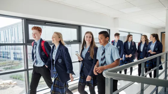 School students socialise as they walk through a corridor with floor-to-ceiling windows.