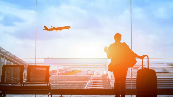 A person watches a plane take off from an airport boarding gate.
