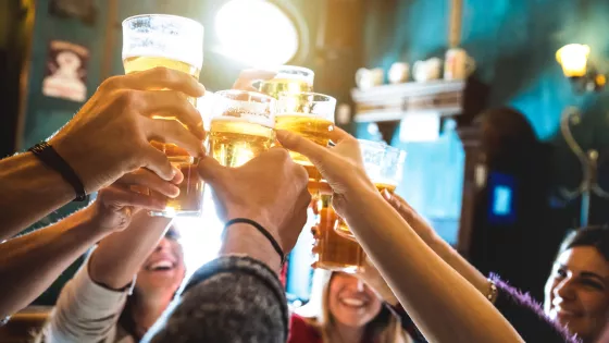 A group of young people cheers with pints of beer in a bar.