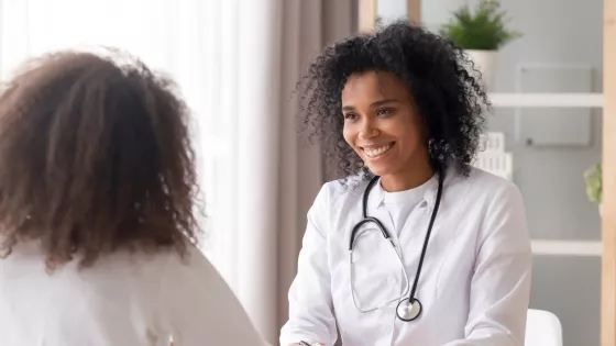 A medical professional smiles at a younger patient during a consultation.