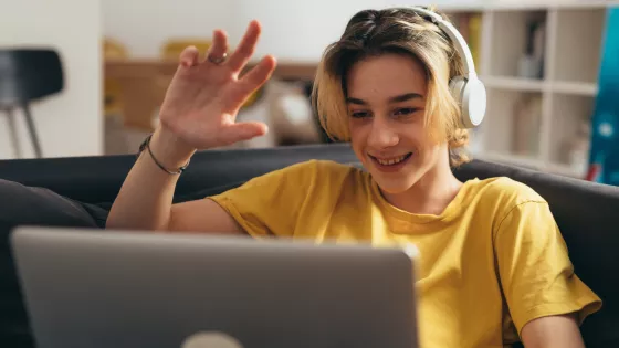 Young boy wearing headphones, waving and smiling on a video call