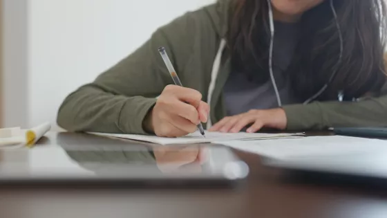 Young girl writing on a piece of paper wearing headphones