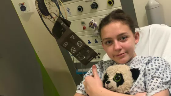 Young girl on hospital bed, clutching a soft toy.