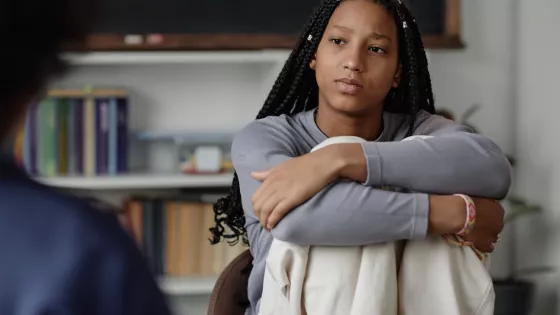 Teenage girl looks serious, with her arms wrapped around her knees