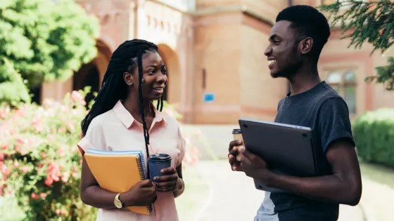 young male and female chat at a university campus with notebooks and coffee in hand.
