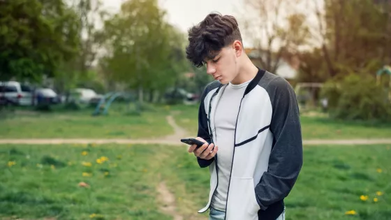 Young boy looks solemnly at his phone outside