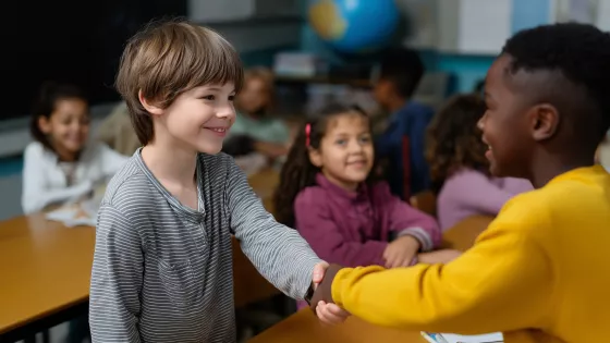 Children shake hands over a school table