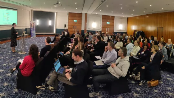 A large group of researchers listen to a lecturer using slides at a research retreat with Young Epilepsy.