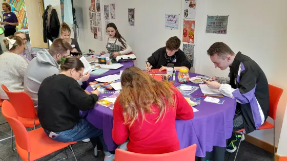 A group of young people from Young Epilepsy sit at a table putting together a pamphlet.