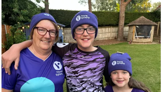 Zac stands between two family members in a garden, all wearing Young Epilepsy beanies.