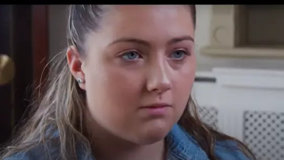 A young woman, Amelia, looks seriously behind the camera.