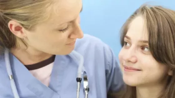 A female medical profession has her arm around a young girl in support.