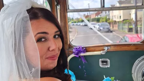 A young woman, Laura, smiles in a wedding dress from the front seat of a vehicle.