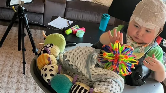 A young boy with bandages from brain surgery plays with colourful toys.
