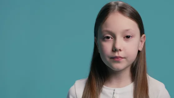 Young white girl stands in a light t-shirt against a blue backdrop.