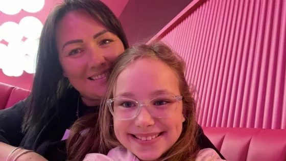 A mother and her daughter smile in a selfie against pink wallpaper.