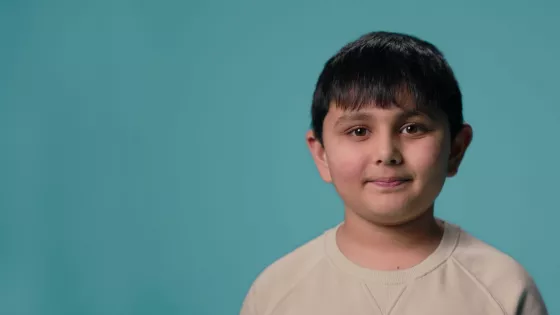 Young Asian boy smiles as he's talking, against a blue backdrop