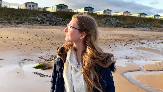 A young woman on a beach looks into the sun.