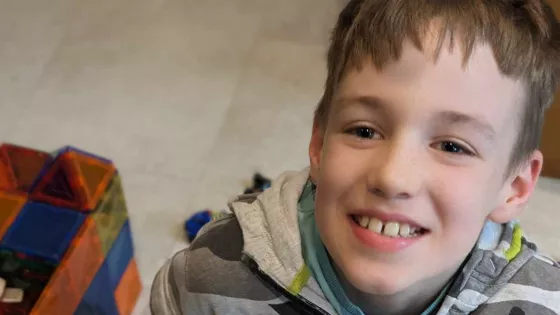 A young boy with a toy block set smiles widely.