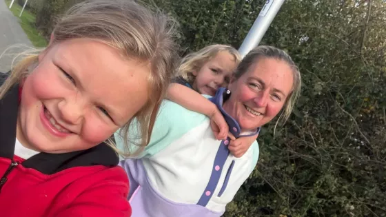 A mother and her two daughters smile in a selfie on a walk.